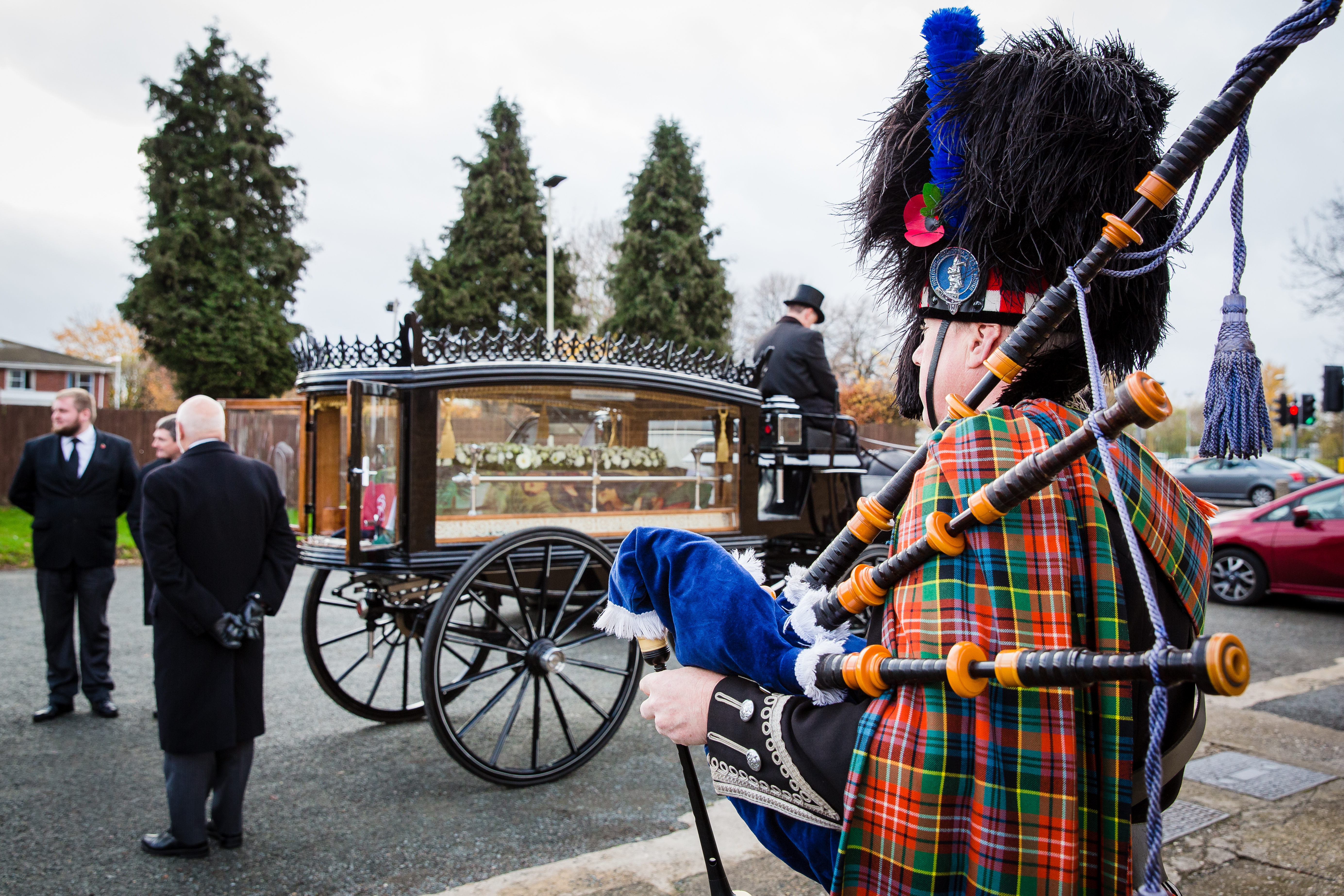 Image of a man holding bagpipes standing next to a horse drawn hearse