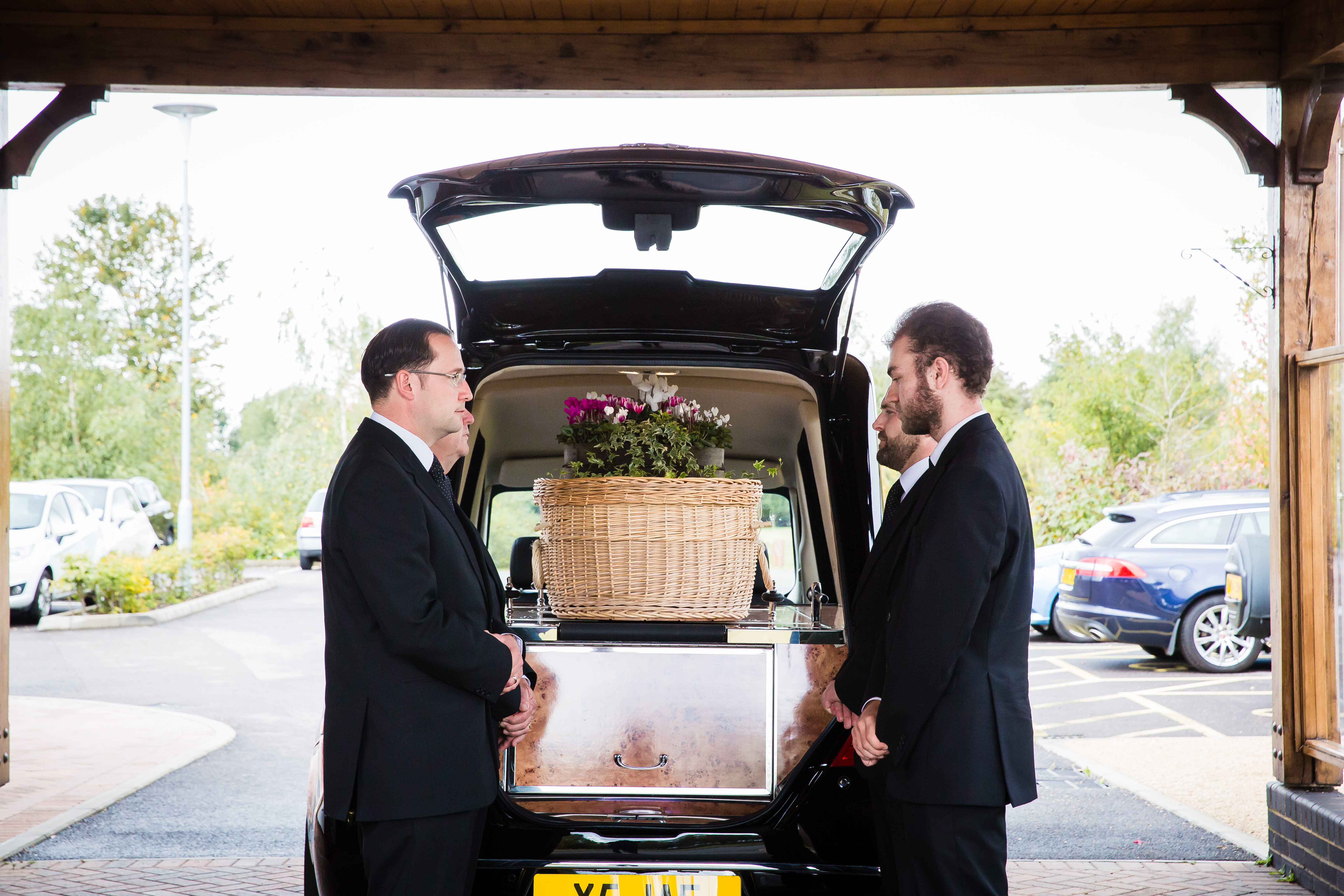 Pallbearers waiting at the rear of the hearse to remove the casket